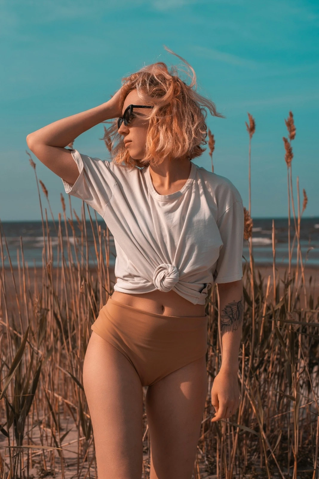 A woman standing in a field near the ocean with wind in her hair, expressing confidence, freedom, and natural beauty